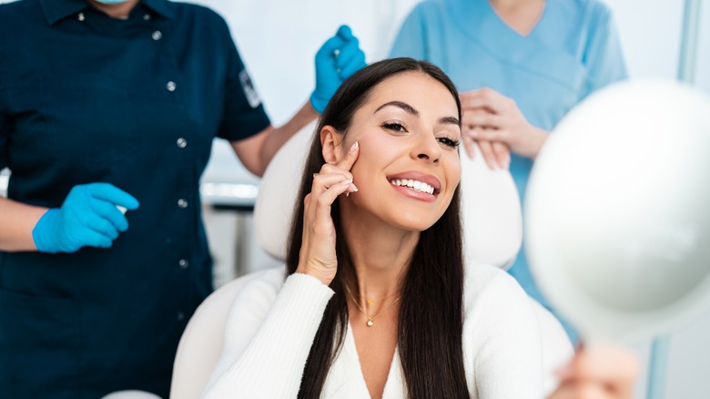 Woman smiles int the mirror at a filler appointment