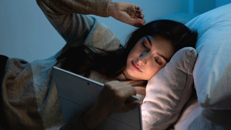 Woman looks at tablet in bed