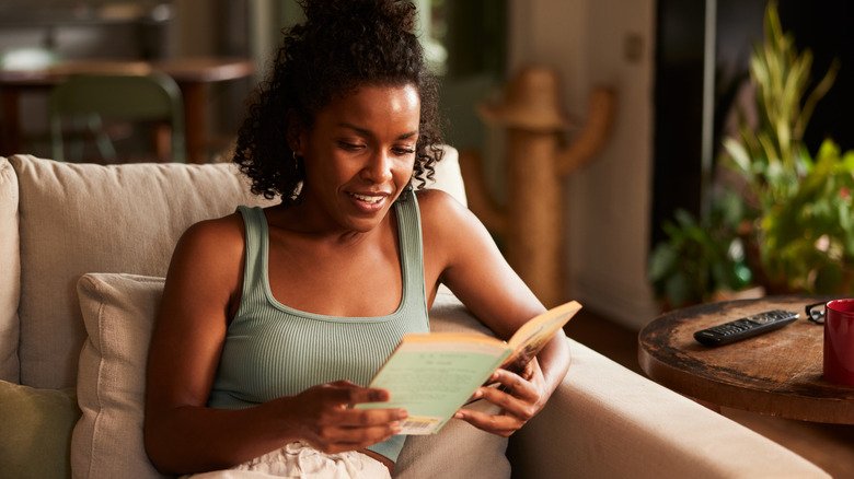Curly-haired woman smiling while reading a book on the couch