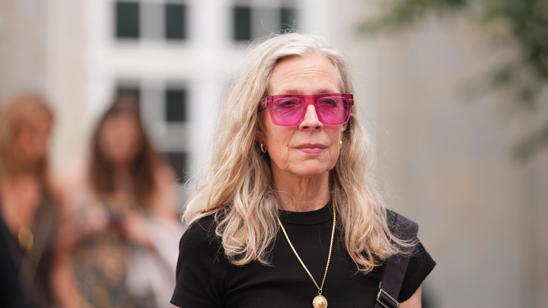 A woman with gray hair wearing pink sunglasses and a black top