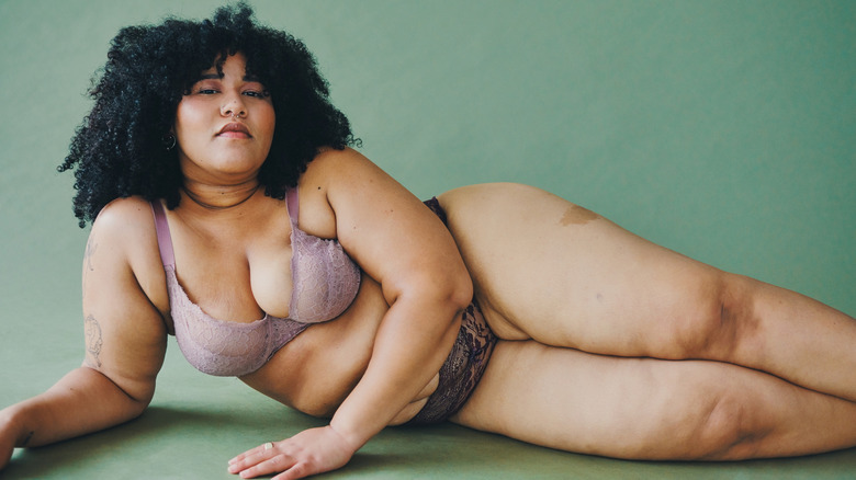 Woman lying on the ground in lace underwear with green backdrop