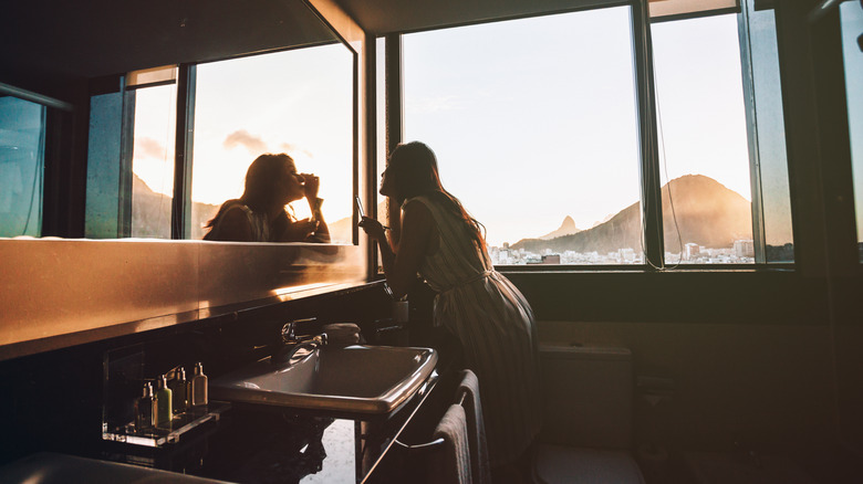 woman applying makeup in hotel room mirror