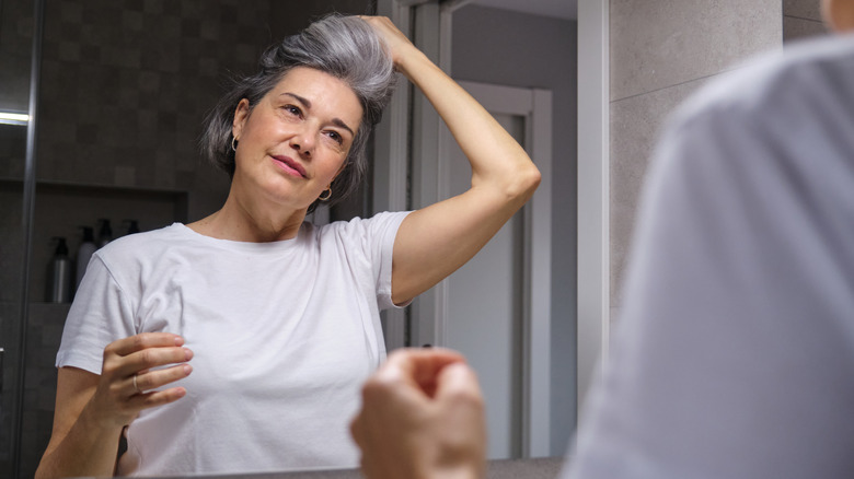 Woman flipping salt and pepper hair, looking at it in the mirror