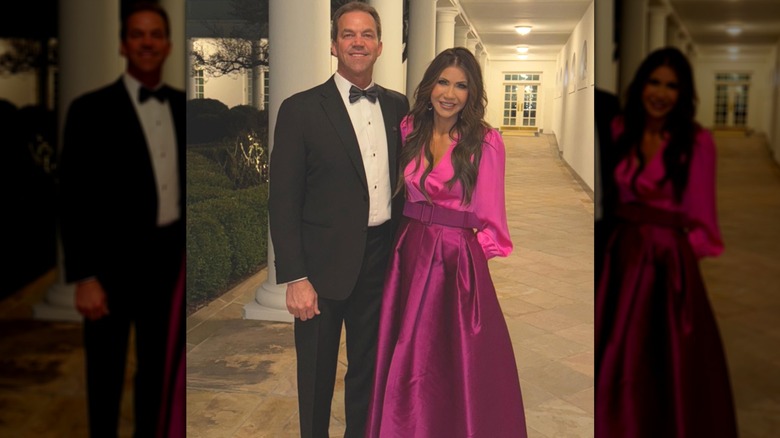 Kristi Noem in a pink dress standing next to her husband Bryon Noem in an outdoor corridor of the White House