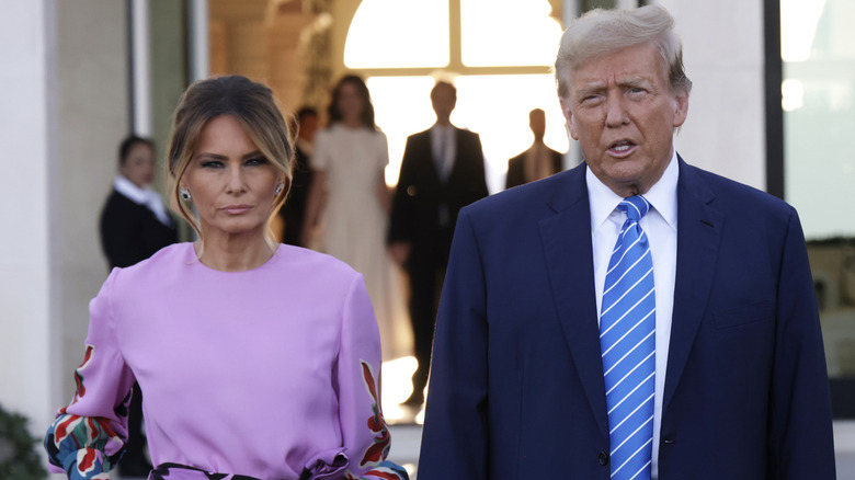 Melania Trump in a purple dress and Donald Trump in a blue suit outside