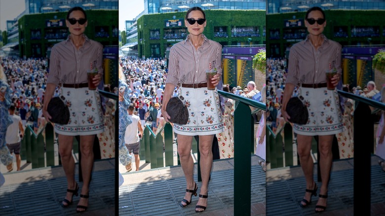 Minnie Driver wearing a stripped button-down shirt, patterned shorts, and holding a cocktail
