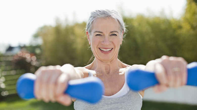 A mature woman holding out two small hand weights