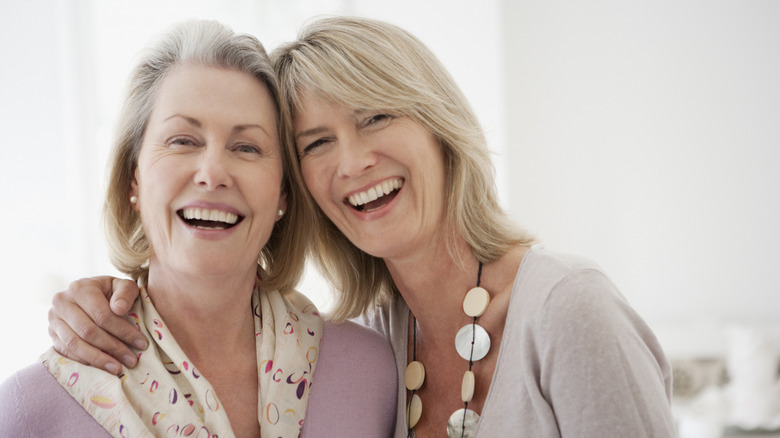 Two mature woman laughing with their arms around one another