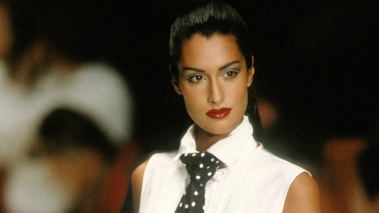 Yasmeen Ghauri in a white sleeveless blouse with a polkadot tie and red lipstick