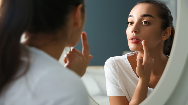 Young woman applies lip cream in mirror