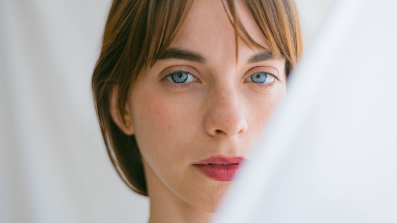 A woman looking through a white curtain with light eyes