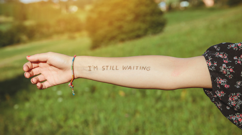 A woman's arm featuring a lettered tattoo reading "I'm still waiting" 
