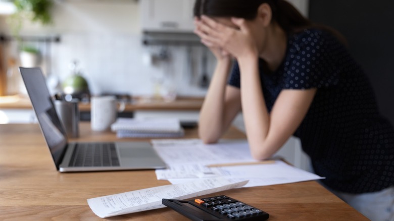 Woman holds her head in her hands while doing bill payments