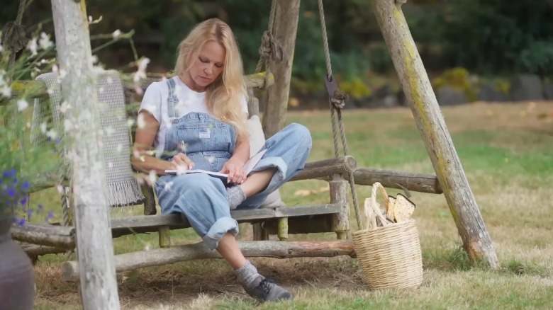 Pamela Anderson sitting in overalls on park swing