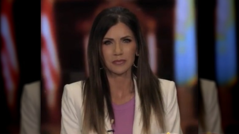 A photo of Kristi Noem on television in a white blazer and straightened hair