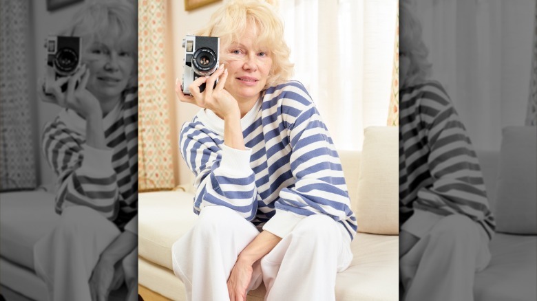 Pamela Anderson smiles with a camera in one hand