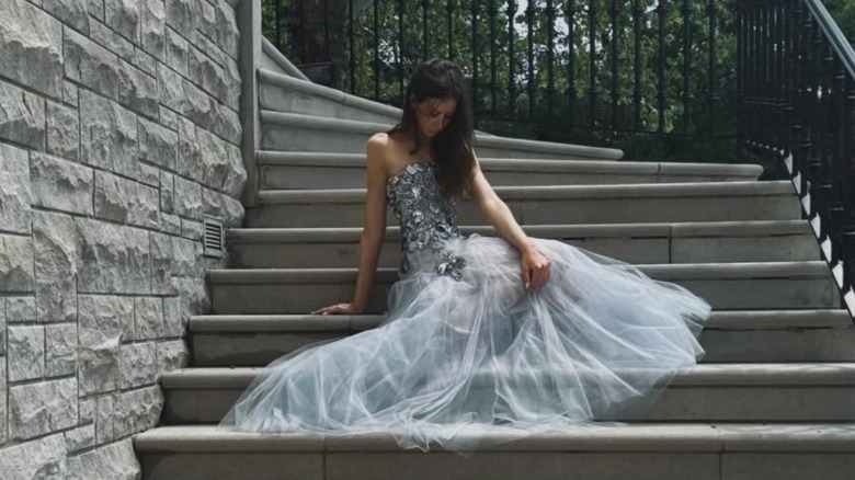 A teen girl sitting on outdoor steps in a strapless silver gown with a tulle skirt